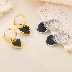 Détail de boucles d'oreilles cœur en émail noir finitions or et argent sur tissu texturé