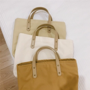 Three minimalist canvas tote bags in beige, white, and tan colors with leather handles
