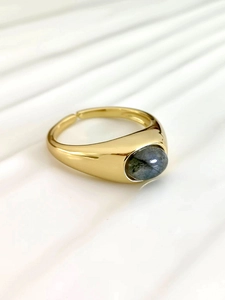 Macro detail of gold adjustable ring with oval grey moonstone on textured background