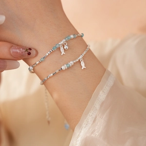 Detail of double-layer silver bracelet with blue beads, pearl and small fish charm