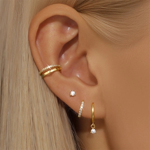 Detailed close-up of a golden earring set with sparkling zircons worn on a model's ear
