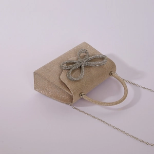 Detail view of a gold glitter evening clutch bag featuring a large rhinestone bow decoration