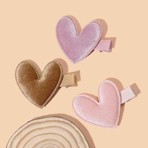 Detailed view of three soft velvet heart hair clips in pink and brown on a beige background