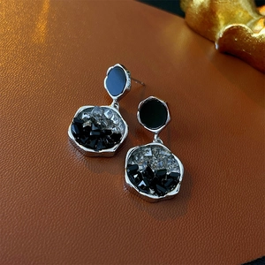 Close-up of irregular crystal drop earrings with silver needles and black stone inlay