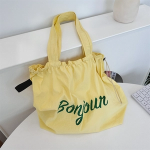 Detail of yellow canvas tote bag with green Bonjour print on a white table