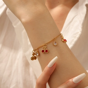 Detailed view of a gold chain bracelet with red cherry pendants and sparkling crystals