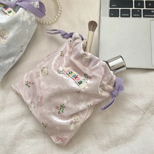Pink velvet drawstring bag with bear print styled with cosmetics on cream fabric