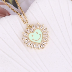 Macro detail of gold heart necklace with zircon border and green enamel smiley face pendant