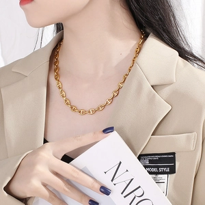 Close-up of gold pig nose buckle necklace worn by model against beige suit background