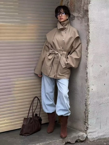 Detail shot of beige trench coat with wide lapels and belt paired with blue jeans