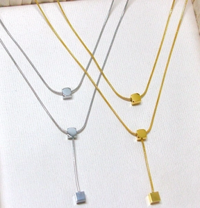 Close-up of gold and silver layered necklaces with cube pendants on textured fabric
