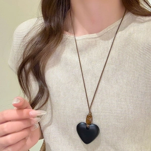 Detailed close-up of a resin heart pendant necklace with amber bead on a brown cord