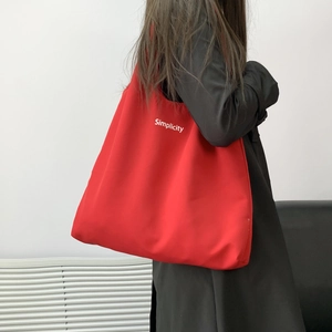 Detail of red canvas tote bag with Simplicity print worn over a black jacket