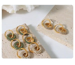 Close-up of gold geometric hoop earrings with emerald green and white pavé crystals