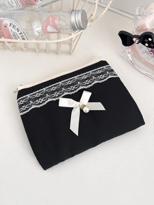 Black fabric coin purse with white lace trim, silk bow, and pearl detail in soft lighting