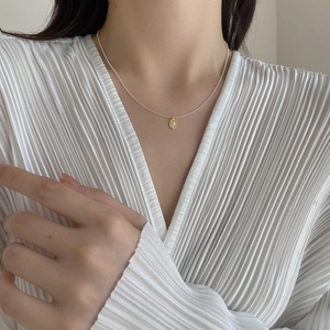 Detail of silver beaded chain necklace with golden oval portrait pendant on model