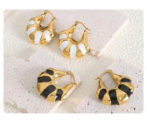 Detail of ribbed C-shape earrings in gold with black and white enamel finishes