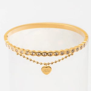 Detailed macro view of golden double-layered heart bracelet with cubic zirconia and love charm