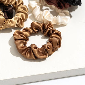 Detail showing various colors of smooth satin scrunchies in cream and earth tones