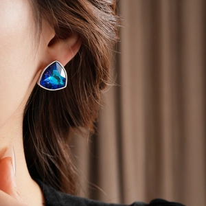 Gros plan détaillé d'un mannequin portant une boucle d'oreille triangle en cristal bleu