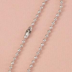 Détail macro d'une chaîne à billes en acier argenté avec fermoir sur tissu rose