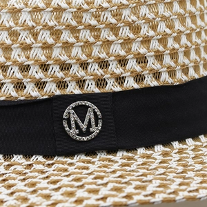Detail of woven straw hat featuring a black ribbon and rhinestone M letter logo emblem