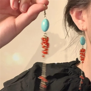 Detail view of long beaded tassel earrings with green oval stone and red dangling beads