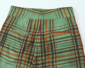 Detailed view of plaid trousers with green and orange checks and symmetric back pockets