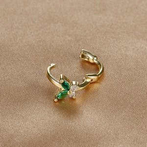 Macro detail of a gold cartilage hoop with green stones and a clear gemstone flower