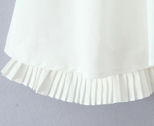 Close-up of white halter dress featuring precise pleated hem and woven fabric texture