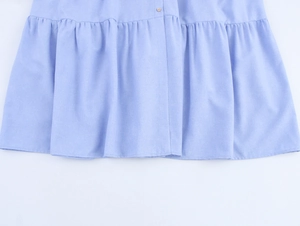 Detail van lichtblauwe linnenlook jurk met geplooide zoom en knoopstiksels