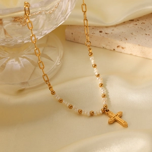 Detail of freshwater pearl necklace with gold cross pendant on beige silk fabric