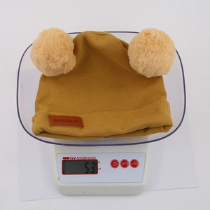 Yellow knit baby winter hat with double plush pom-poms weighing 53g on scale