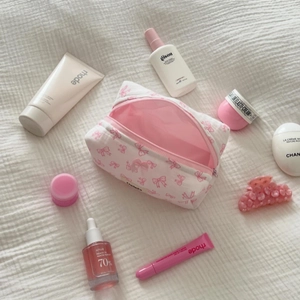 Flat lay of open white bow pattern makeup bag with pink lining and skincare products