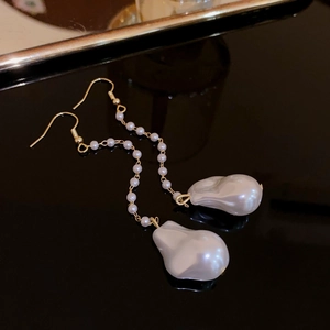 Macro detail of gold metal chain earrings with elegant baroque pearl pendants on black background