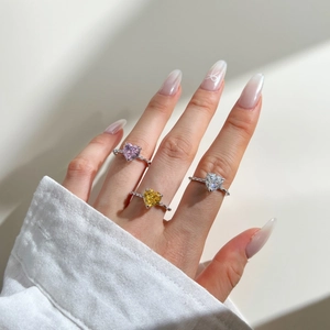 Detailed view of three heart-shaped gemstone rings in pink, yellow, and clear on hand