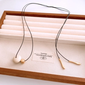 Detail of wax cord necklace featuring white resin pendant and gold ball on fabric