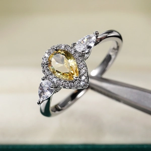 Detailed macro view of pear-cut yellow zircon ring with halo diamond setting and silver band