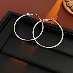 Close-up of polished silver hoop earrings on a black display with gold light reflections