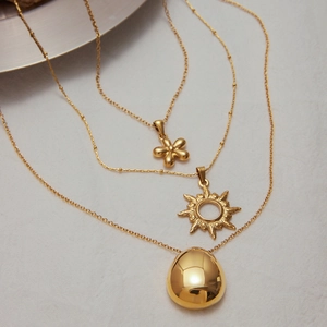 Detail of layered 18k gold stainless steel necklace with sun and flower pendants