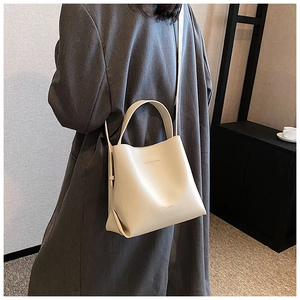 Detailed view of beige leather bucket bag with top handle and shoulder strap on model