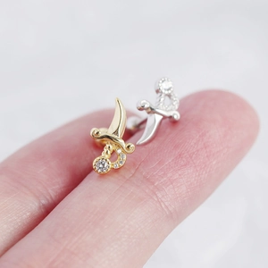 Macro view of tiny gold and silver dagger stud earrings with cubic zirconia on fingertips