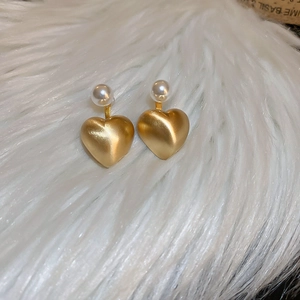 Macro detail of matte gold heart earrings with white pearl studs on plush white background