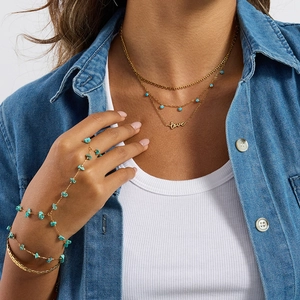 Layered gold necklace with love charm and turquoise hand chain ring set on denim