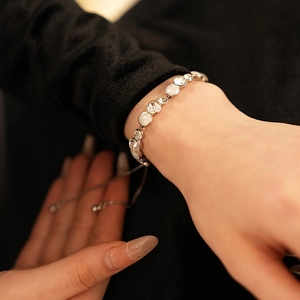 Détail du bracelet réglable en argent avec breloques en émail blanc sur le poignet