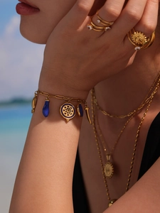 Close-up of golden bracelet with blue enamel fish charms on female wrist at the beach