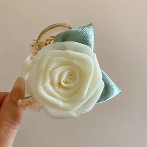 Vue détaillée de la pince à cheveux fleur en tissu blanc avec feuilles en soie verte