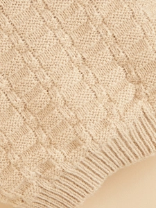 Close-up of beige knitted pet sweater with classic checkerboard texture and ribbed cuffs