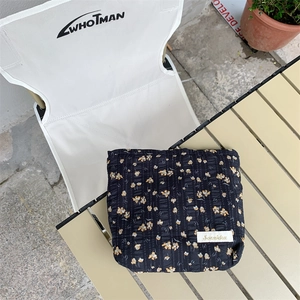 Detail of floral quilted cosmetic bag with yellow daisies on black fabric surface