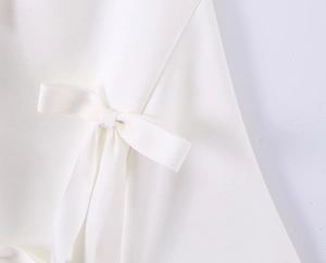 Detail shot of pearl white woven fabric with a matching ribbon bow decoration